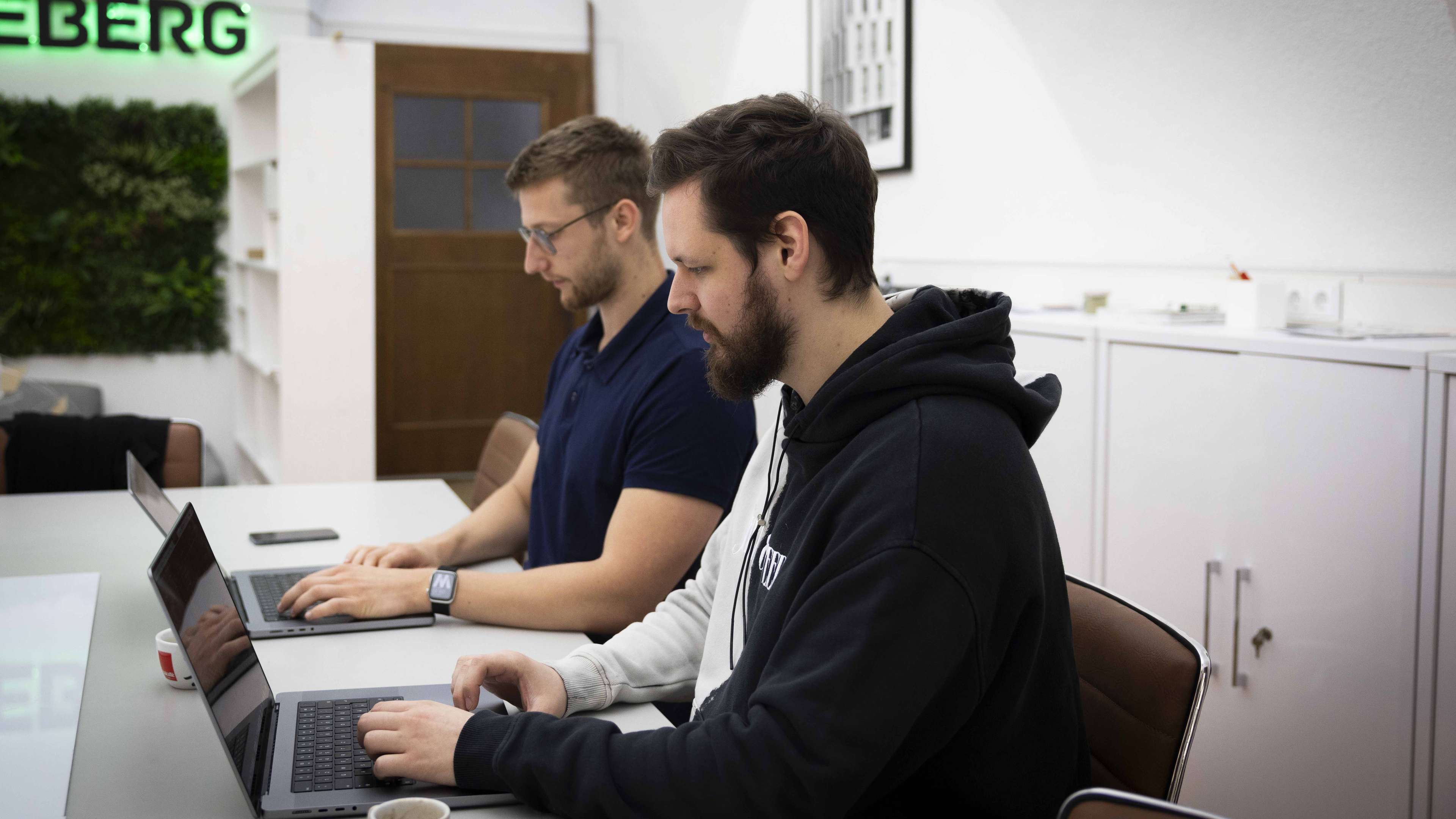 Zwei junge Männer sitzen nebeneinander und arbeiten an ihren Laptops