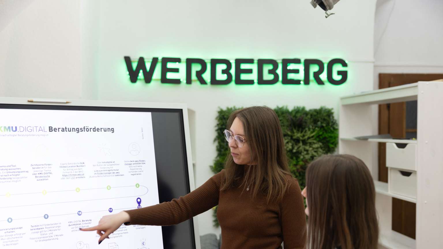 Zwei junge Frauen stehen an einem Bildschirm und reden über die Grafik.