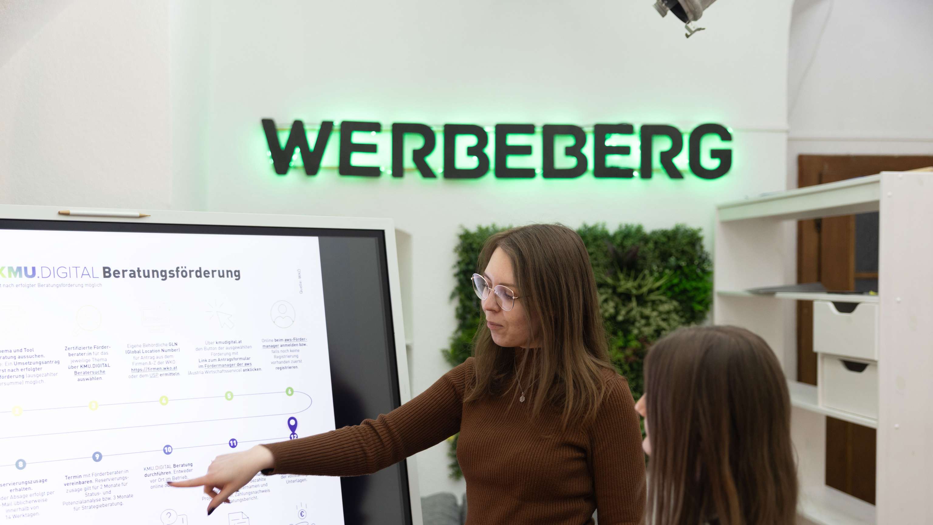 Zwei junge Frauen stehen an einem Bildschirm und reden über die Grafik.