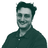 A person with curly hair, wearing glasses, and a collared shirt, against a plain background.