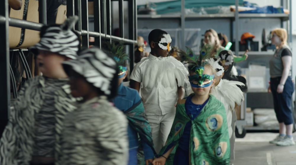 group of children backstage at a show in full animal costumes featuring zebras, a peacock and an eagle