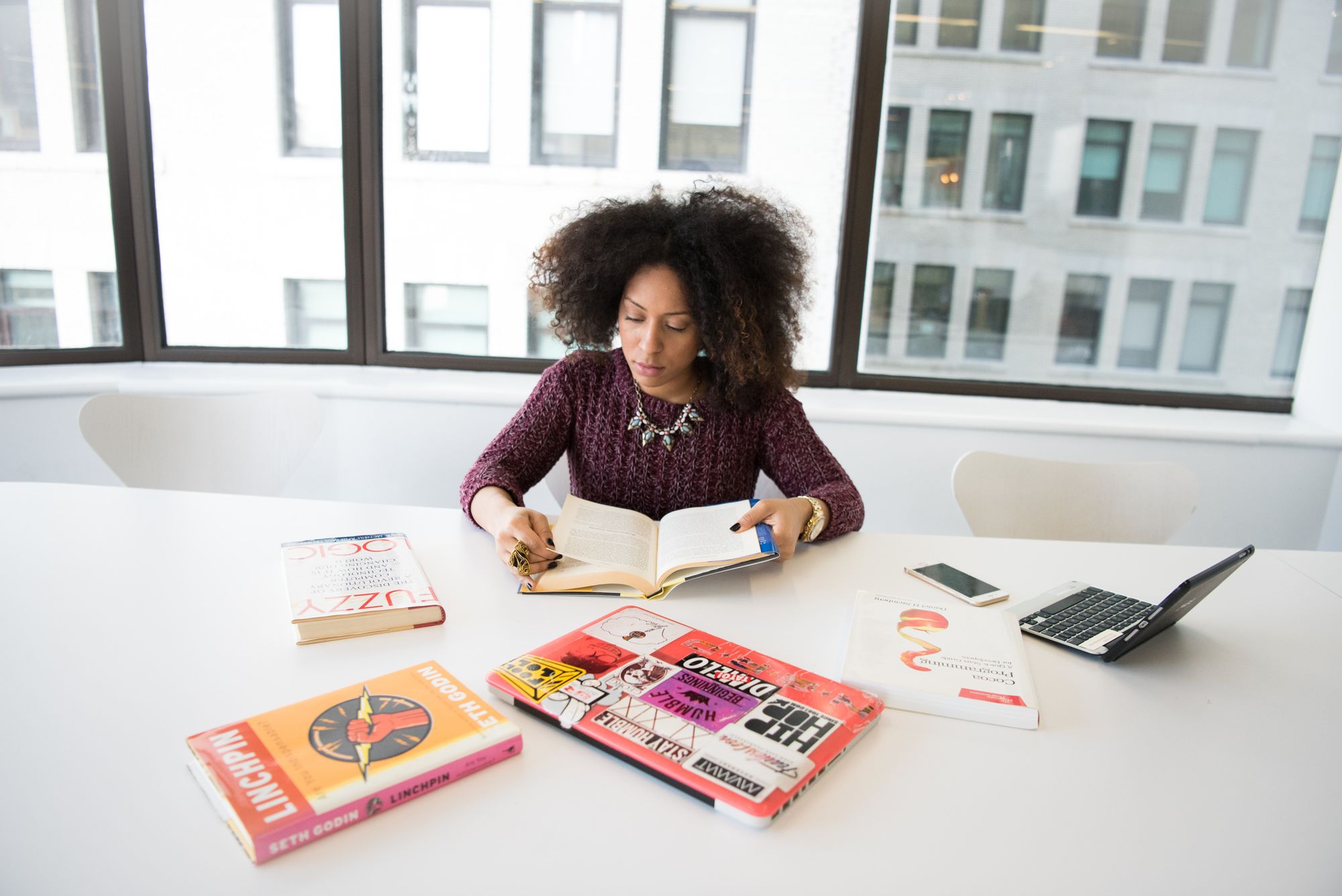 Woman reading a book, seated at an office table with skyscrapers behind her