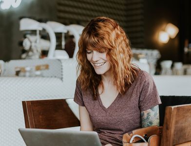 Woman in purple shirt typing in a restaurant and enjoying remote work benefits