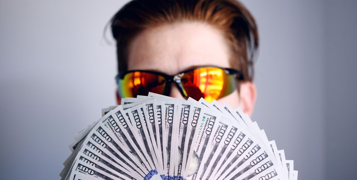 Photographer in sunglasses holding a fan of hundred American dollar bills
