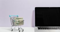 Dollar bills in a mini-trolley beside an open laptop to symbolize international payroll