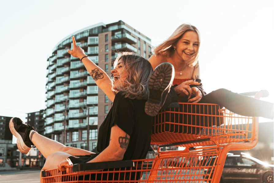 2 young women laughing whilst riding in orange shopping trolleys