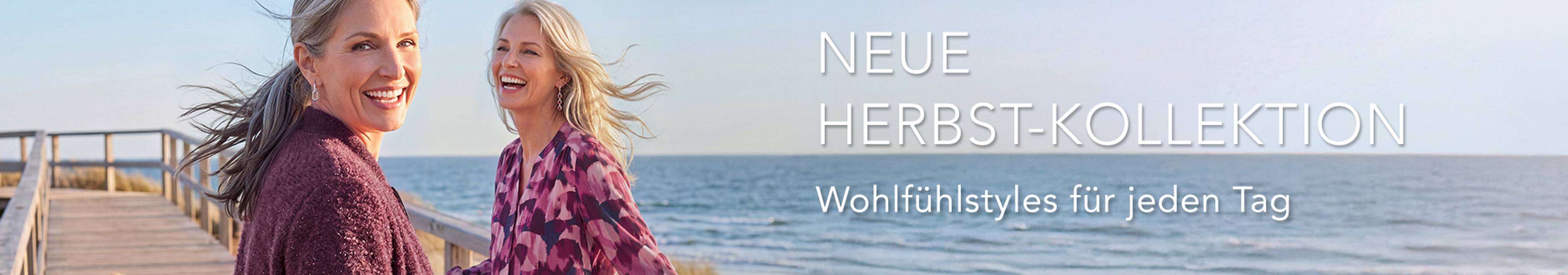  Zwei Frauen in gemütlicher Herbstkleidung lächeln und spazieren auf einer Strandpromenade. Text: „Neue Herbstkollektion. Wohlfühlstyles für jeden Tag.“