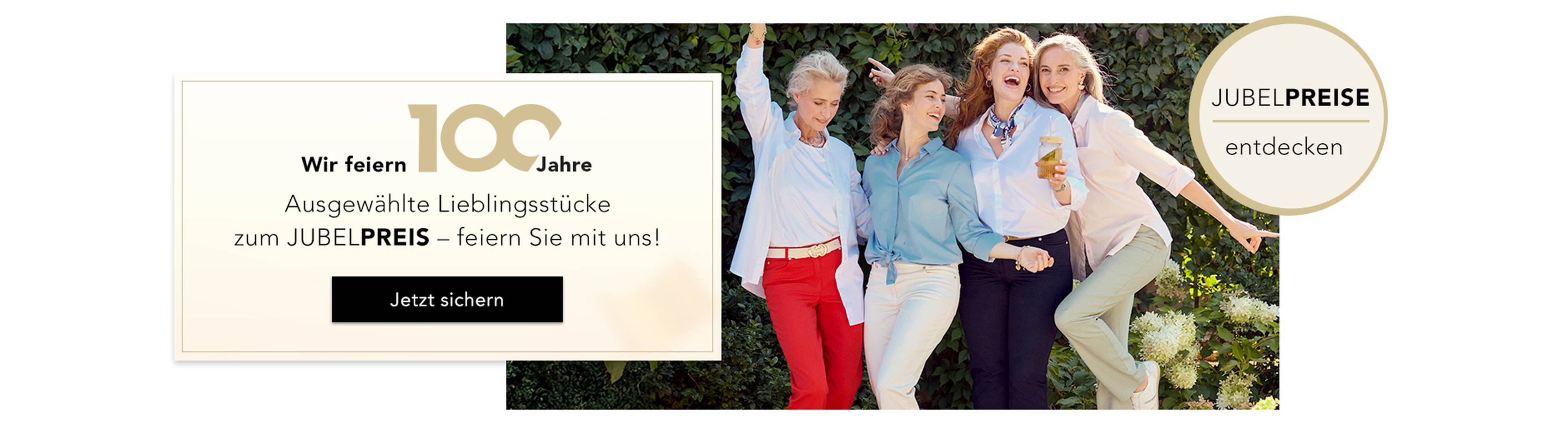Eine Gruppe von Frauen feiert fröhlich in schicken Outfits; auf einem Banner stehen „100 Jahre“ und „JUBEL-PREISE“.