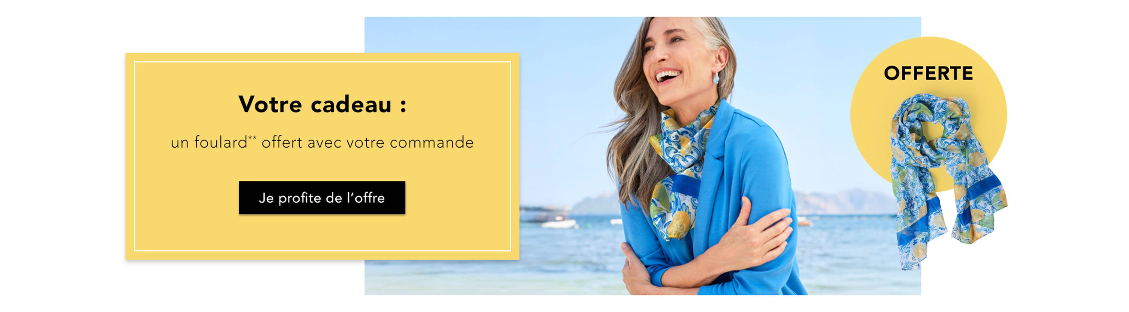 Une femme souriante au bord de la mer, vêtue d'un haut bleu et d'un foulard à fleurs ; à gauche, on peut voir l'offre proposant un foulard gratuit pour tout achat.
