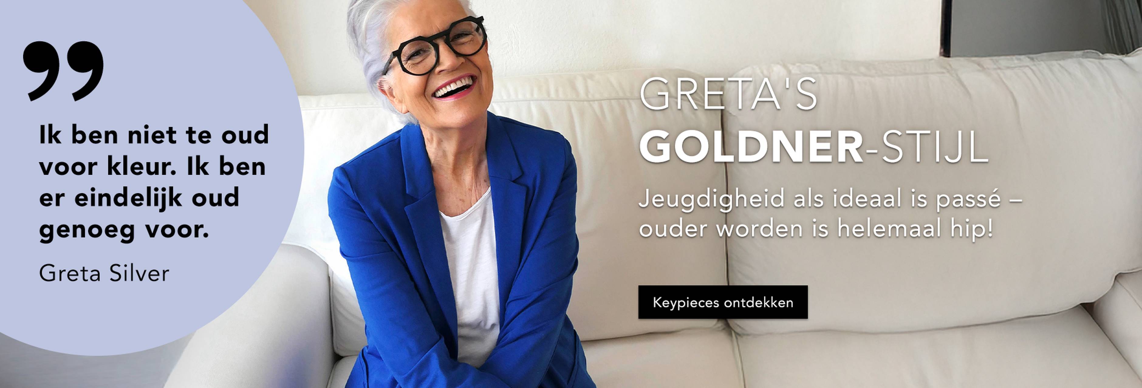 Glimlachende vrouw met grijs haar en een bril, die een blauwe blazer draagt en op een witte bank zit. De tekst straalt zelfvertrouwen uit met betrekking tot leeftijd en stijl en promoot kleding die door Greta Silver wordt aanbevolen.