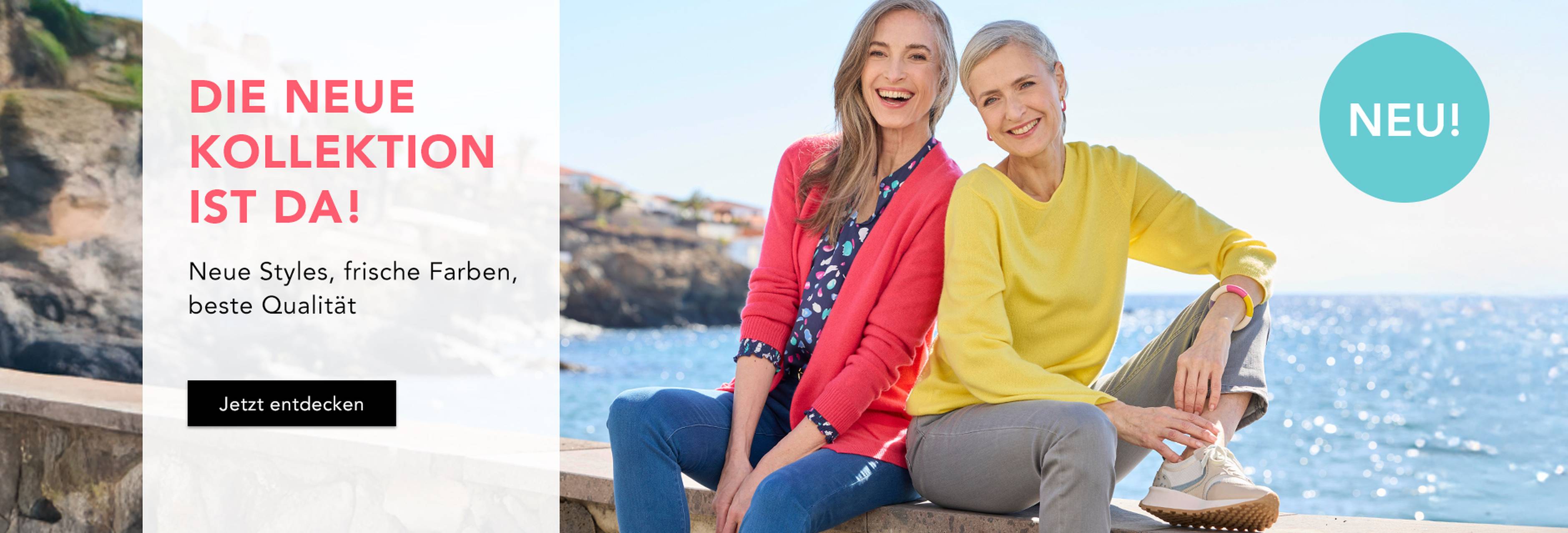 Zwei lächelnde Frauen in gelbem Pullover und pinker Strickjacke am Meer