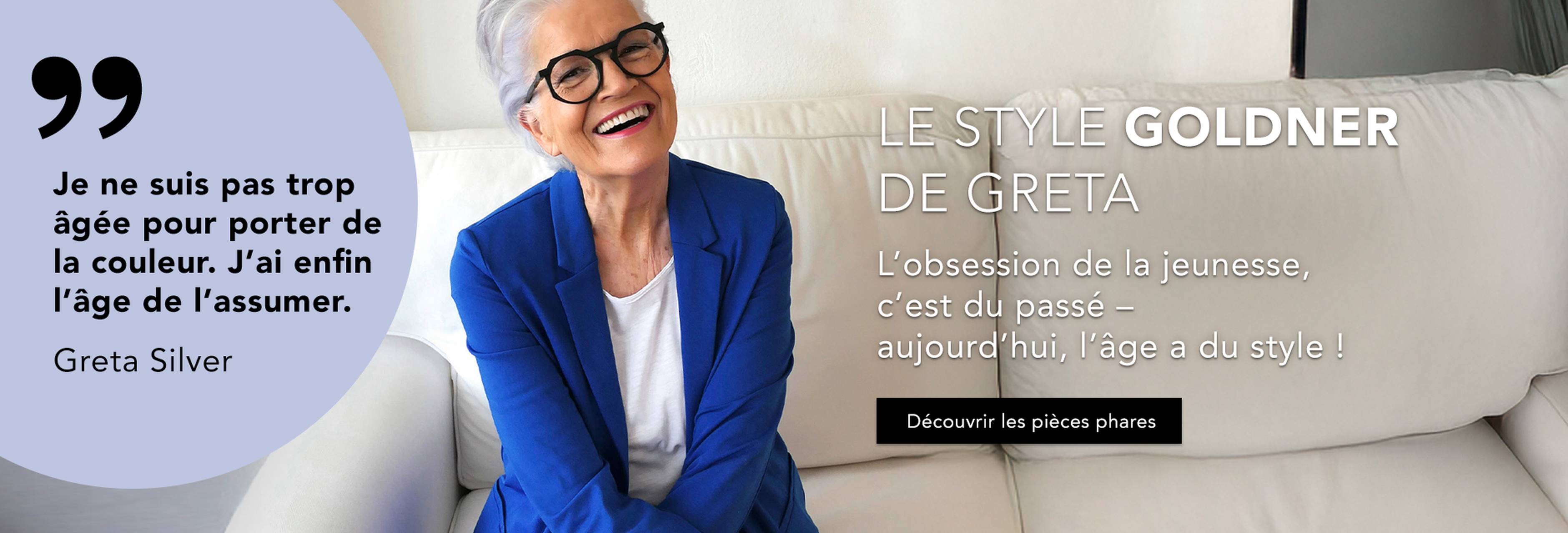 Femme souriante aux cheveux gris, portant des lunettes et un blazer bleu, assise sur un canapé blanc. Le texte transmet une assurance liée à l'âge et au style et fait la promotion de vêtements recommandés par Greta Silver.