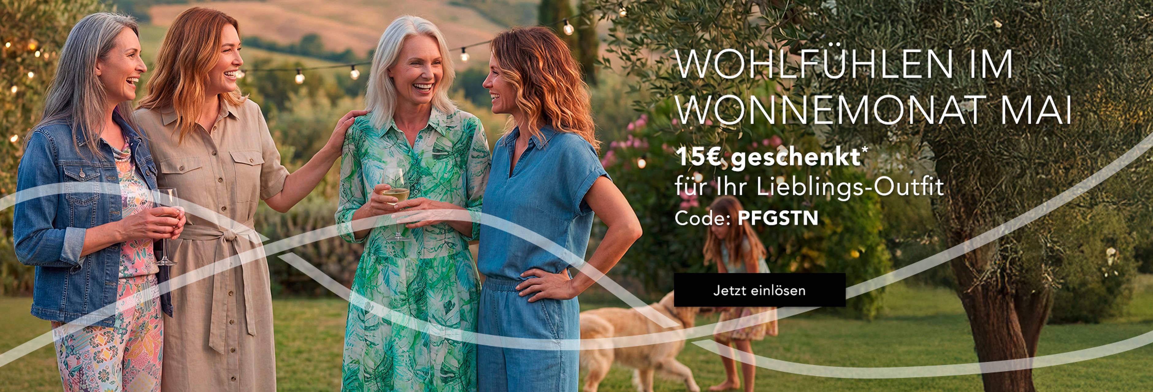 Vier Frauen unterhalten sich fröhlich im Freien in eleganten Kleidern, umgeben von einer üppigen Landschaft. Angebote sind über einen Rabattcode erhältlich.