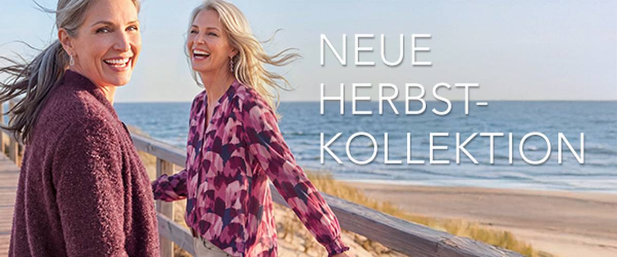  Zwei Frauen in gemütlicher Herbstkleidung lächeln und spazieren auf einer Strandpromenade. Text: „Neue Herbstkollektion. Wohlfühlstyles für jeden Tag.“
