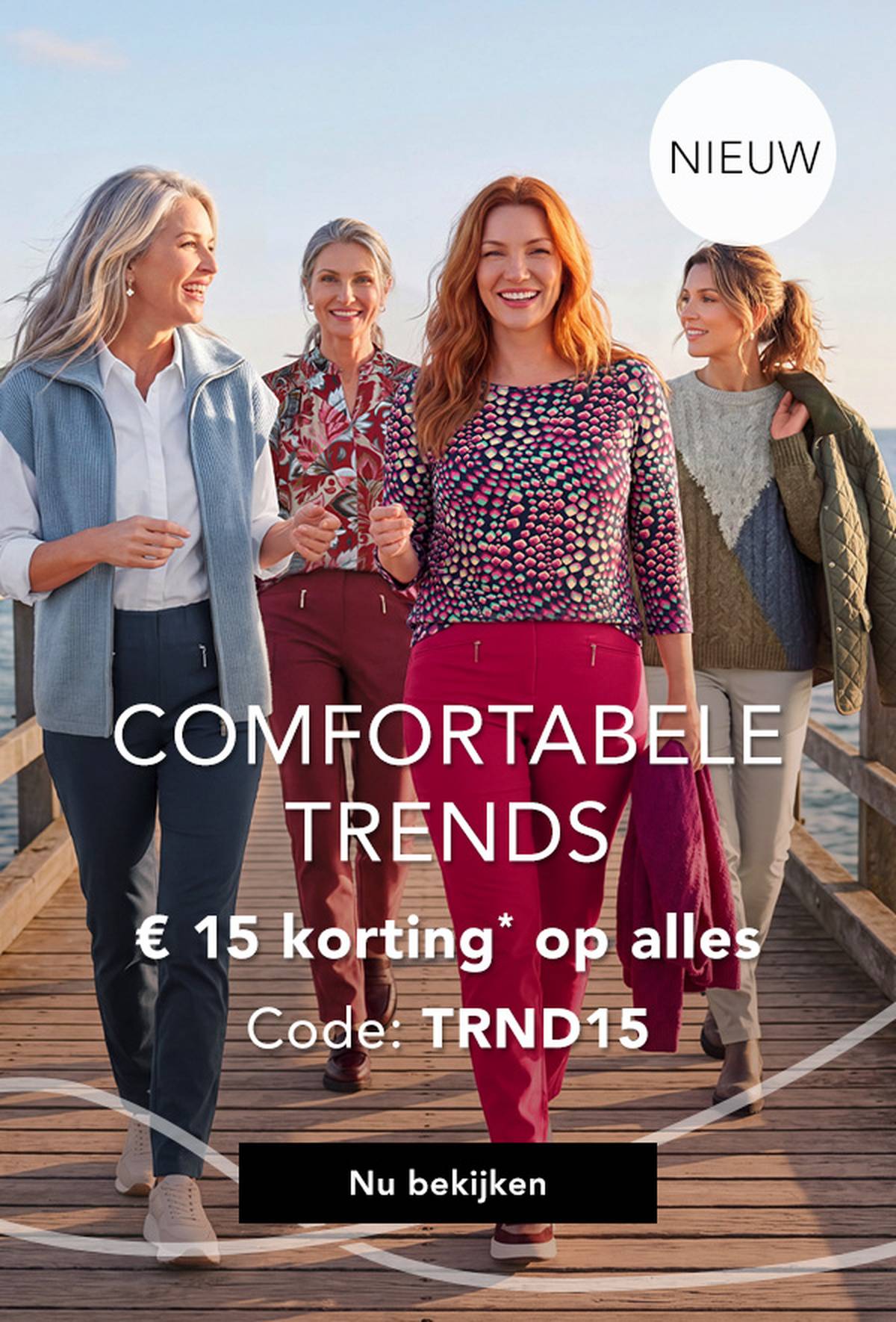Vier vrouwen in stijlvolle, kleurrijke outfits wandelen over een steiger aan zee, lachen en genieten van een zonnige dag.