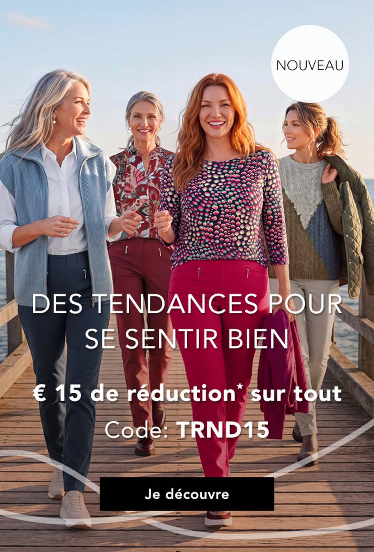 Quatre femmes en tenues élégantes et colorées se promènent sur une jetée au bord de la mer, souriantes, profitant d'une journée ensoleillée.
