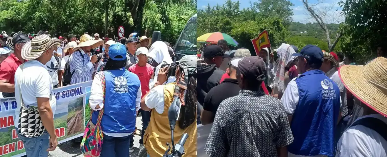 A group of people gathered outdoors, some wearing hats and vests, holding banners and signs, engaging in a discussion or protest.