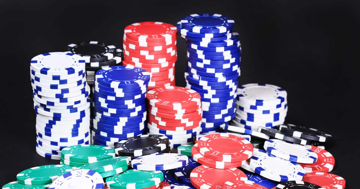 Huge stacks of colorful poker chips, including red, blue, black, green, and white, arranged against a black background.