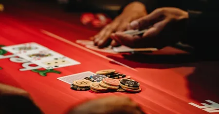 A person's hands arranging poker chips and cards on a red casino table
