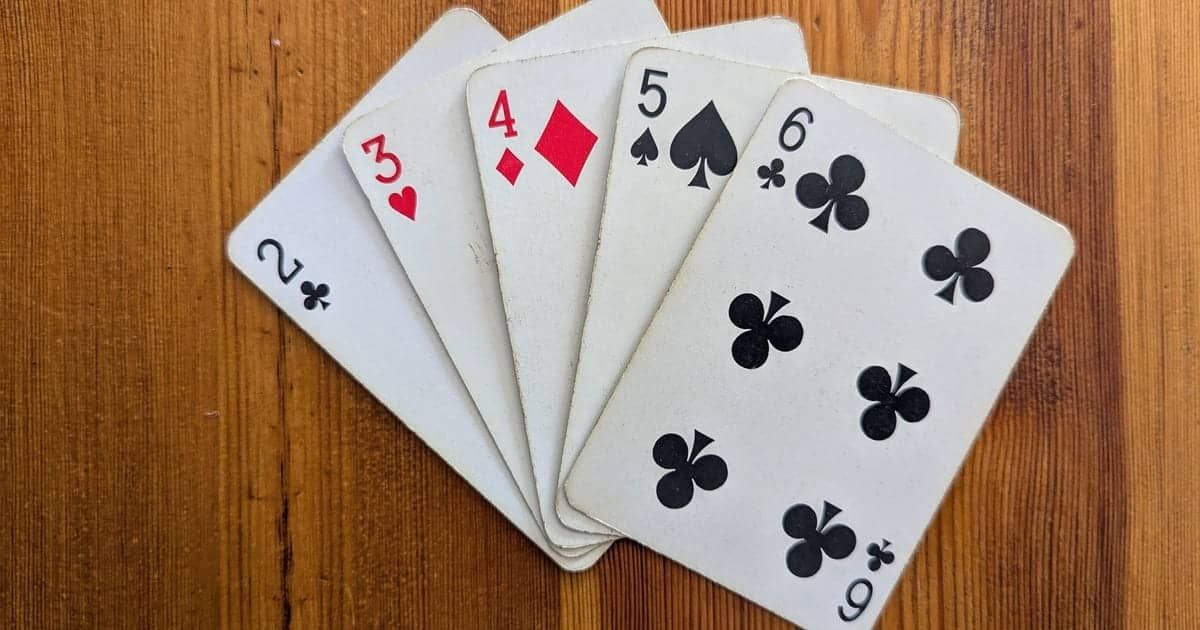 A straight hand with 2 of clubs, 3 of hearts, 4 of diamonds, 5 of spades, and 6 of clubs, on a wooden table