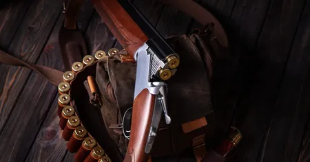 A shotgun with two bullets inside, laid on a rustic background with a brown bag and a strap of shotgun shells.