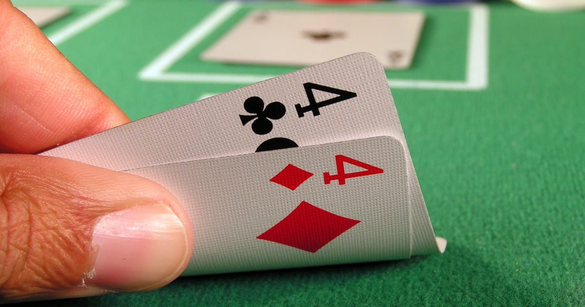 Close-up of a hand holding two playing cards: a 4 of clubs and a 4 of diamonds, on a green felt table.