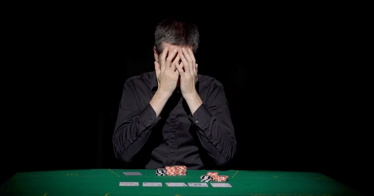Person in a black shirt at a poker table holds their face in frustration, with chips and cards in front of them.