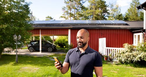 Solcellskund som tittar på sin mobil, ståendes framför sitt hus