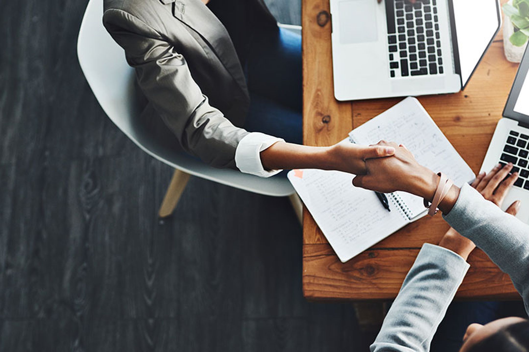 Två personer som sitter vid varsin dator skakar hand