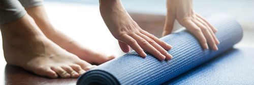 En persons fötter och händer intill en yogamatta