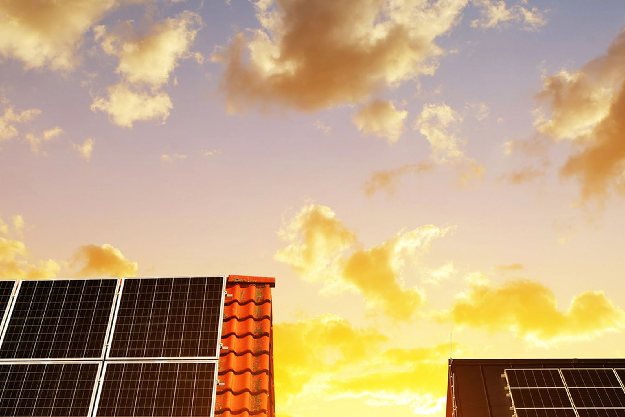 Hustak med solpaneler på med solnedgång i bakgrunden