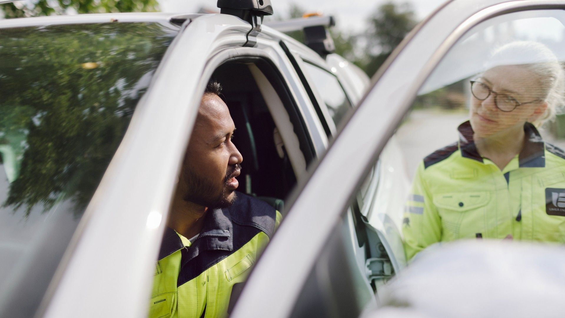 Två personer i varseljackor, en sittandes i bil med öppen förardörr och en utanför