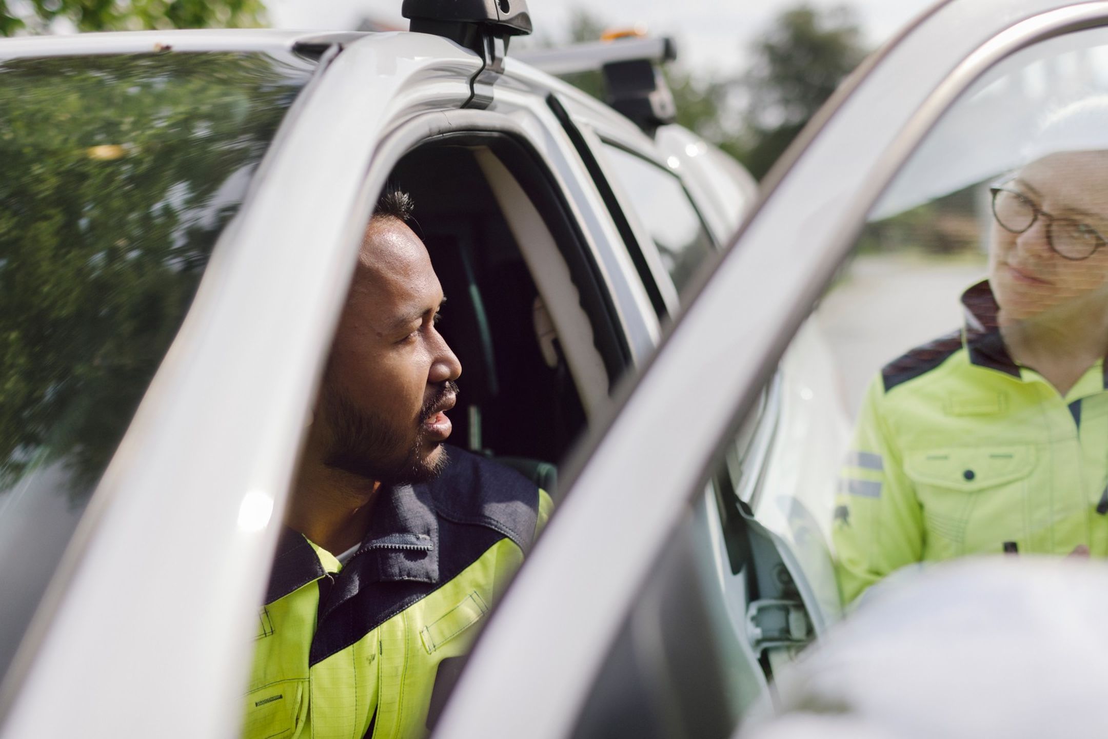 Två personer i varseljackor, en sittandes i bil med öppen förardörr och en utanför