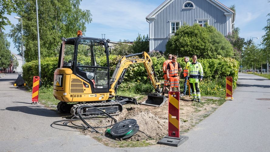 En grävmaskin står vid ett uppgrävt område på en gata.