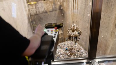 Person som kör kran ses bakifrån styra över stor gripklo med avfall för förbränning