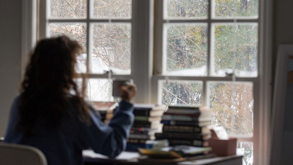 Person sittandes vid ett skrivbord som tittar ut genom ett fönster