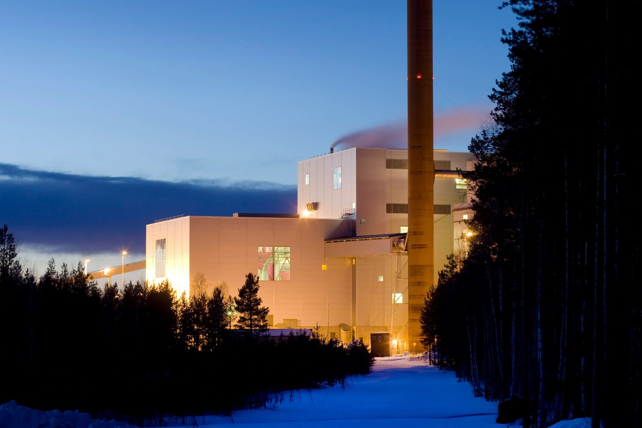Dåva kraftvärmeverk med skog i förgrunden, snö på marken och blå himmel