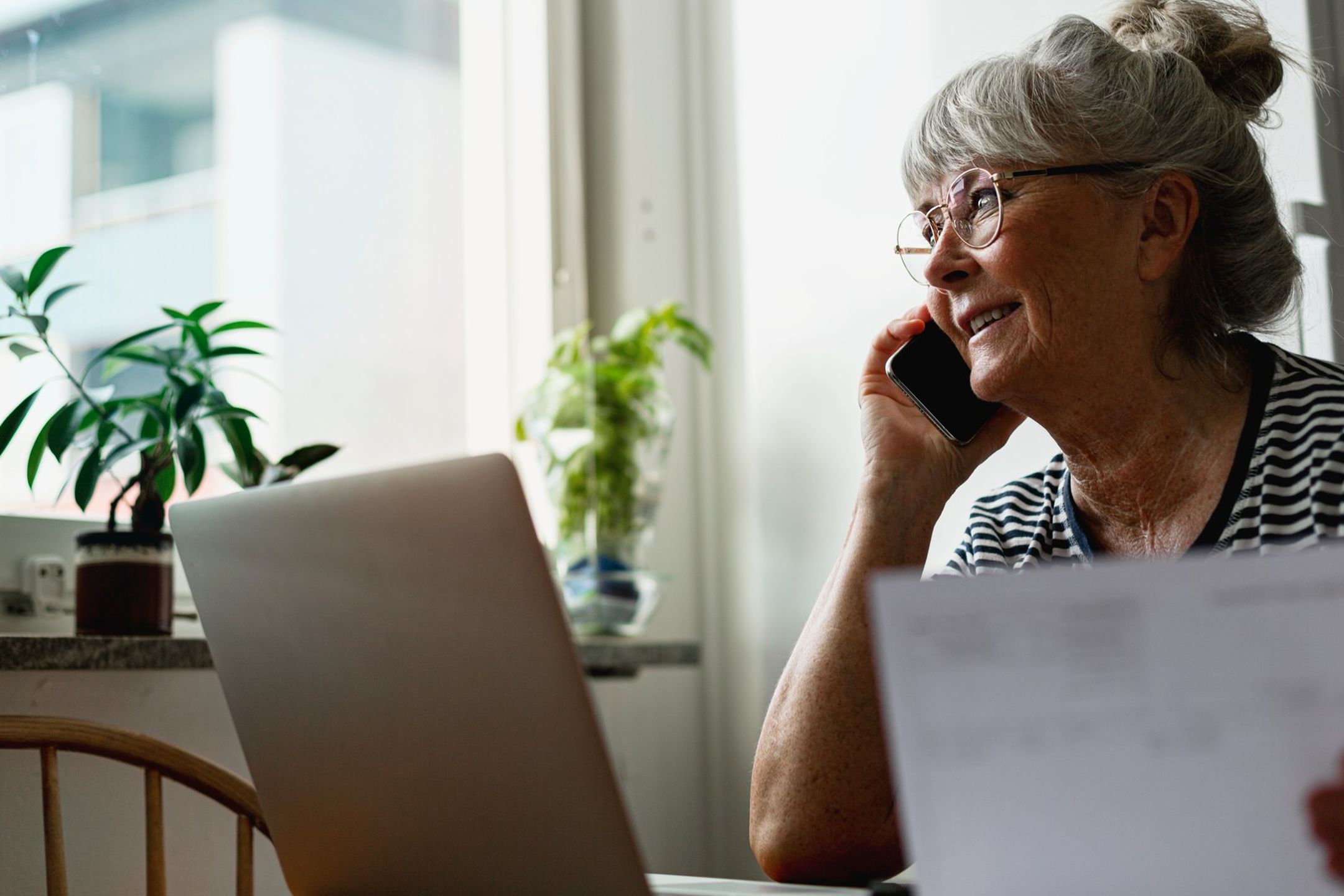 Kvinna sitter vid skrivbord med växter dator och dokument medan hon pratar i telefon