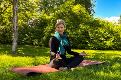 Person som sitter i lotusställning på en yogamatta och tittar in i kameran.