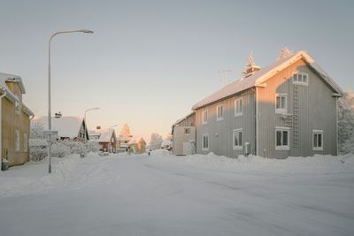 Snöklädd gata med hus på båda sidor, svagt solljus ger sken på byggnaderna