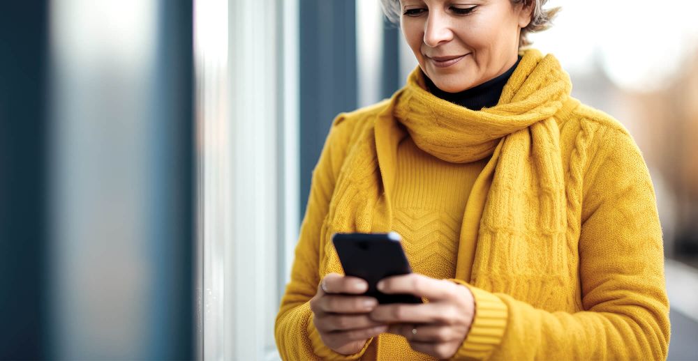 En äldre person i en gul jacka och tröja tittar på sin telefon