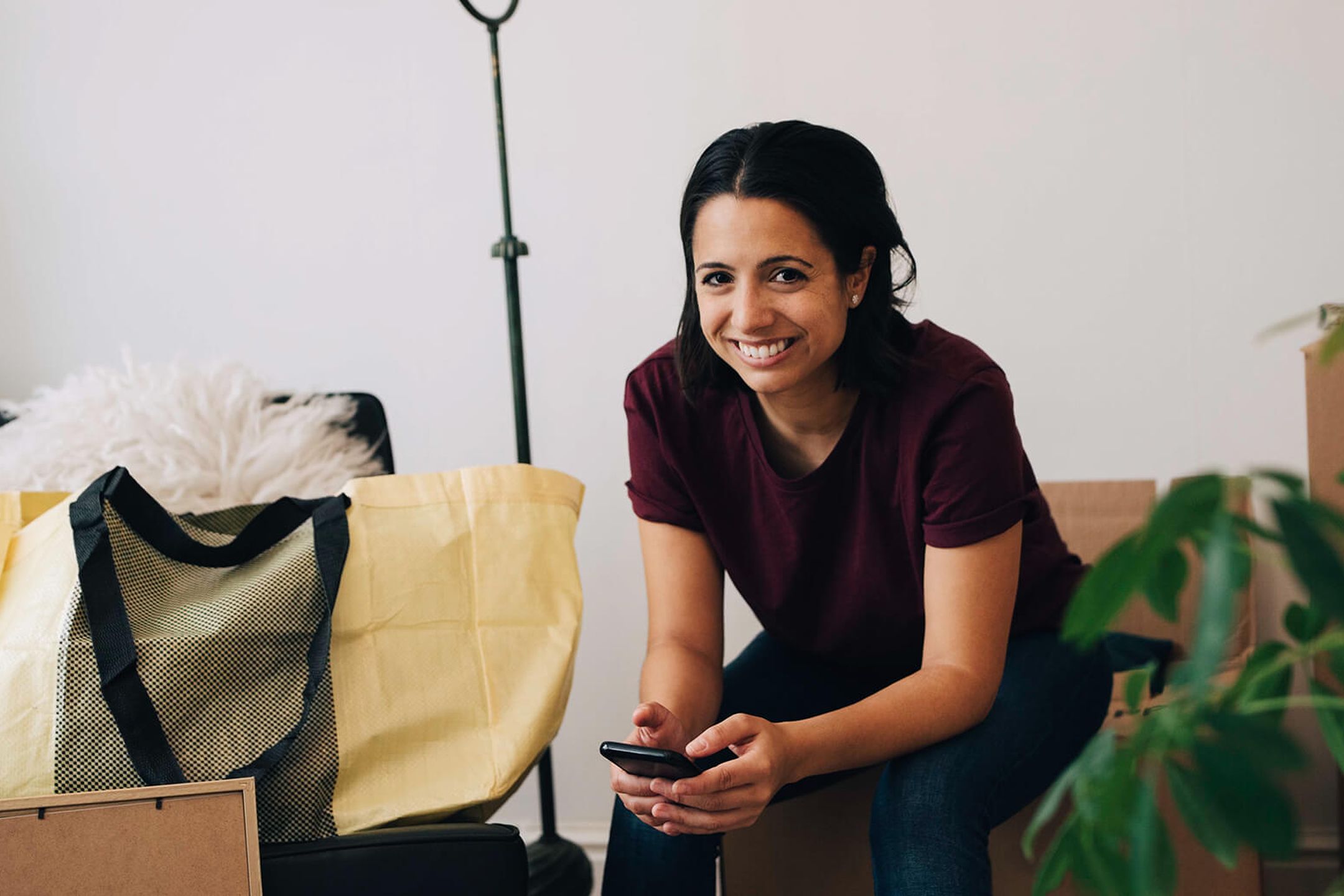 En ung person håller en telefon medan hen flyttar sina saker in i sitt nya boende