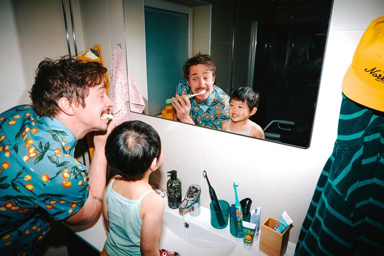 En vuxen och ett barn borstar tänderna framför spegeln och skrattar ihop i badrummet