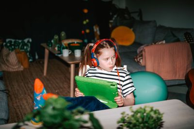 En flicka med hörlurar sitter i soffan och håller en surfplatta, omgiven av lekfull inredning och mjuka färger
