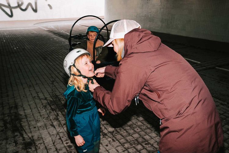 En vuxen sätter på hjälmen på ett skrattande barn vid en lådcykel i en tunnel