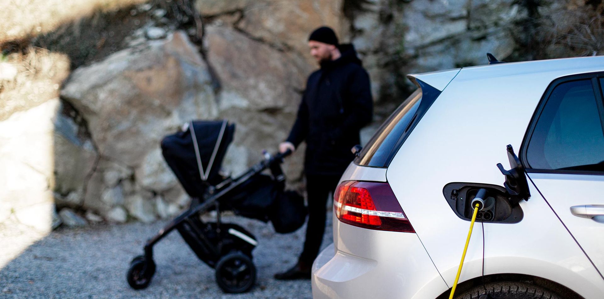 Elbil med förälder och barnvagn i bakgrunden