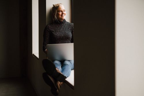 Person som sitter med en latop i knät i ett fönster
