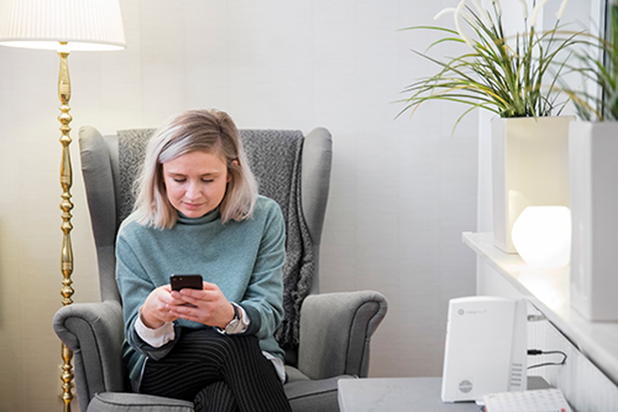 Kvinna sitter i fåtölj och kollar på mobilen
