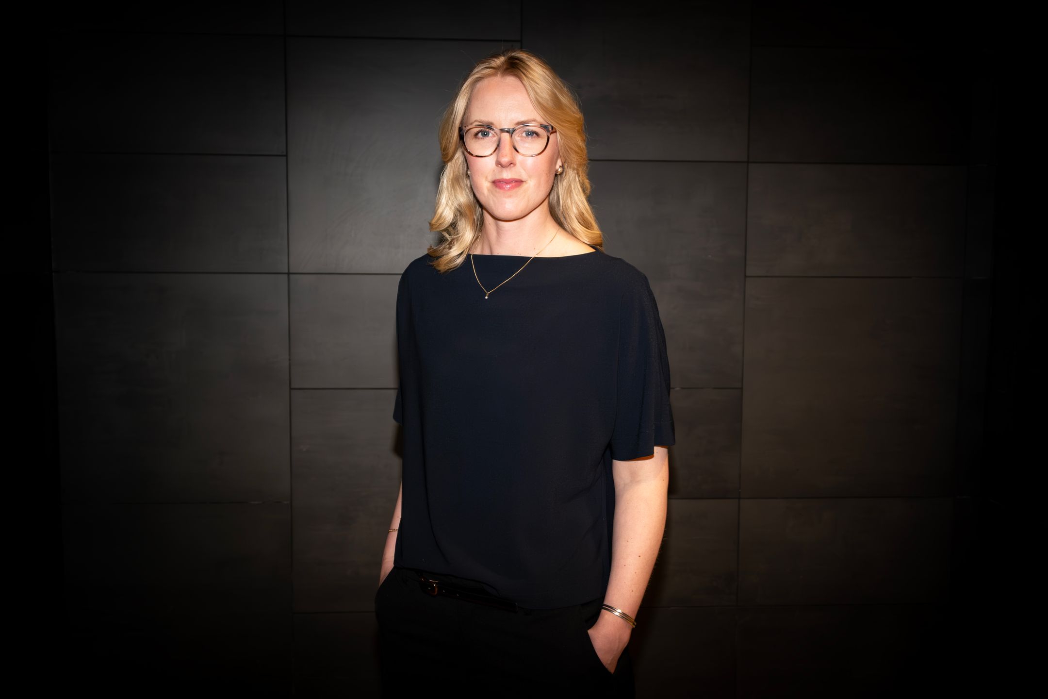 Porträtt av Sara Jonsson, vice vd, stående framför mörk vägg inomhus