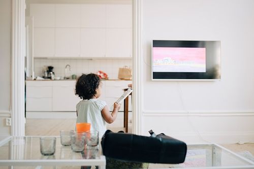 Litet barn som står framför en tv med en fjärrkontroll i handen.